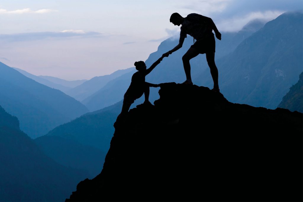 Two people climbing a mountain-top in silhouette