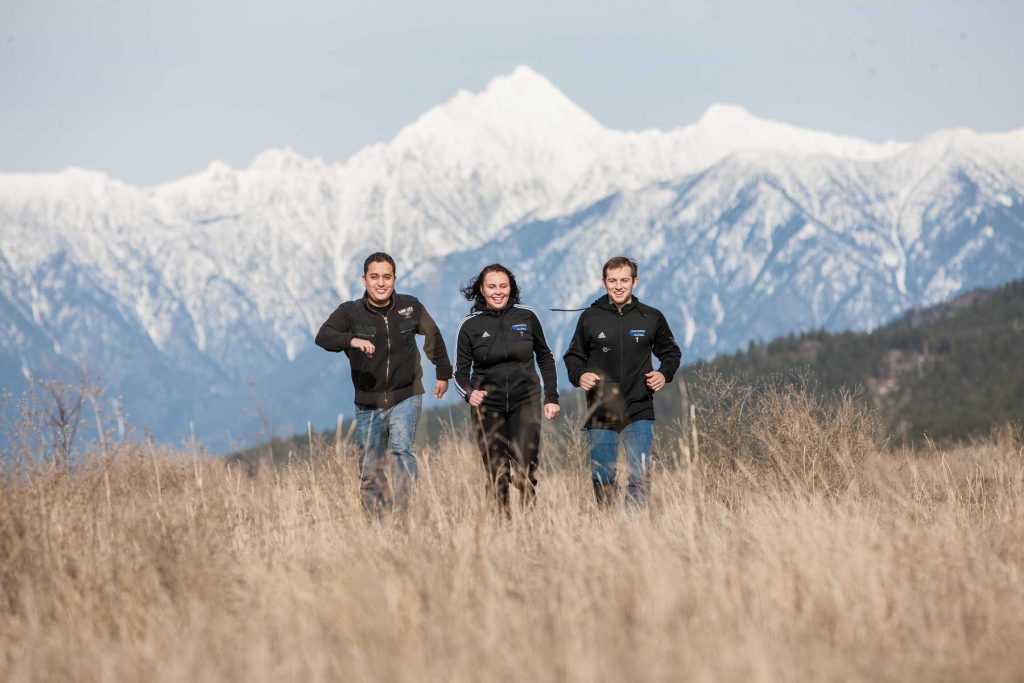 An image of three students running across a fiel with Mt. Fisher in the background.