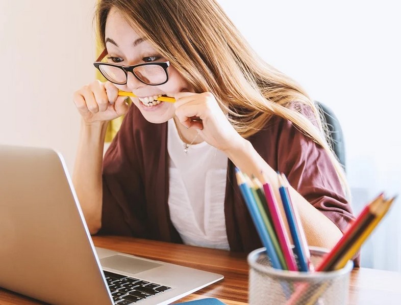 young woman at a computer with pencil between her teeth